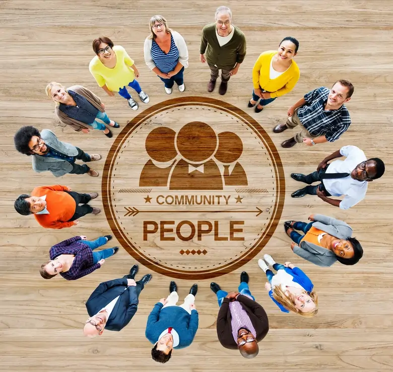 Diverse group of people standing in a circle around a wooden emblem with the words "COMMUNITY" and "PEOPLE," symbolising support and empowerment in a community-focused environment.