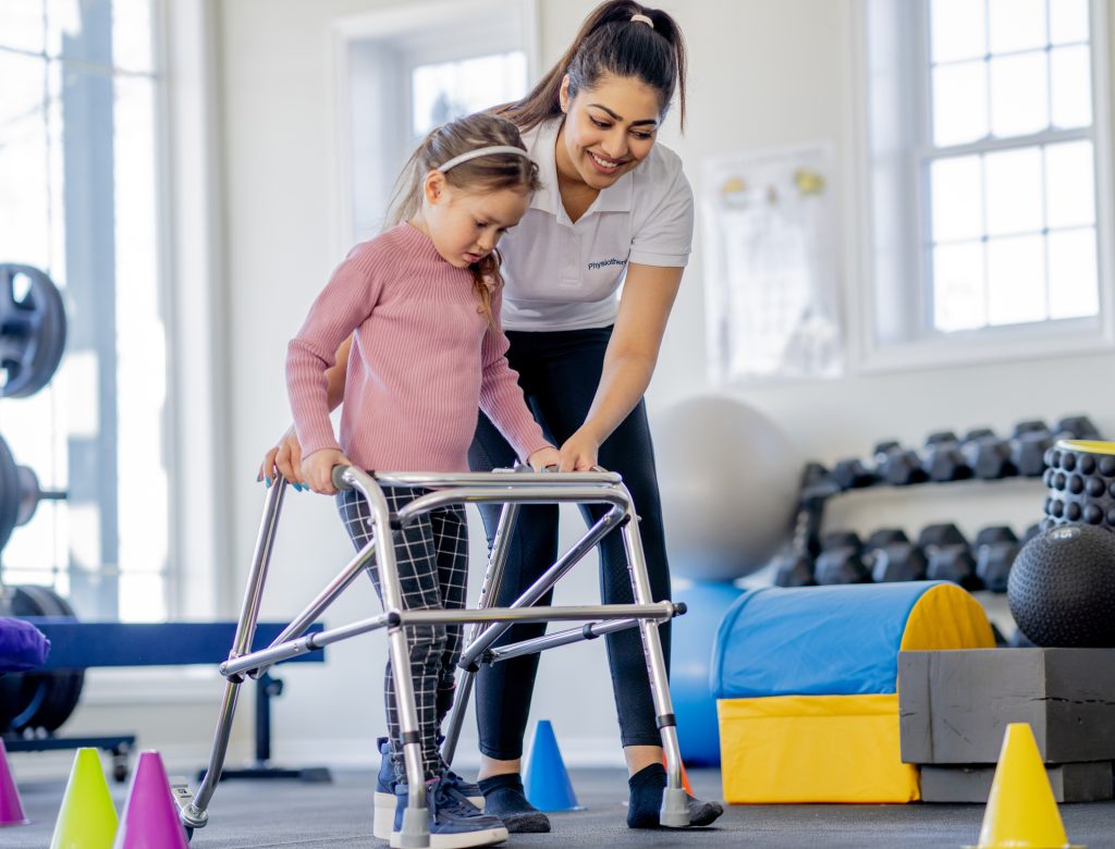 Child using a walker with assistance from a smiling occupational therapist in a supportive therapy environment, focusing on independence and mobility skills.