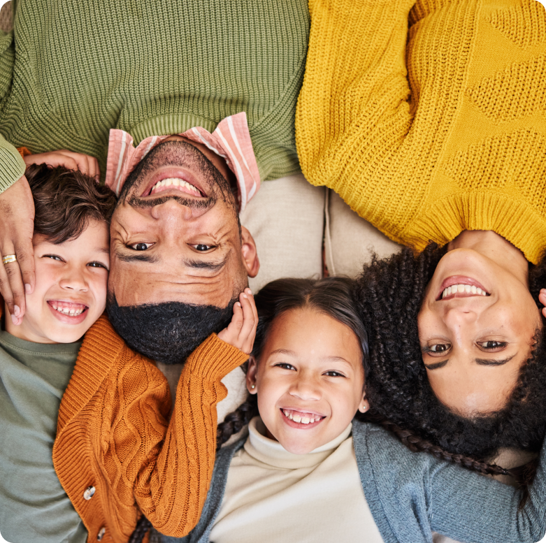 Family enjoying time together on a couch, smiling and displaying warmth, representing community and support in a comfortable living environment.
