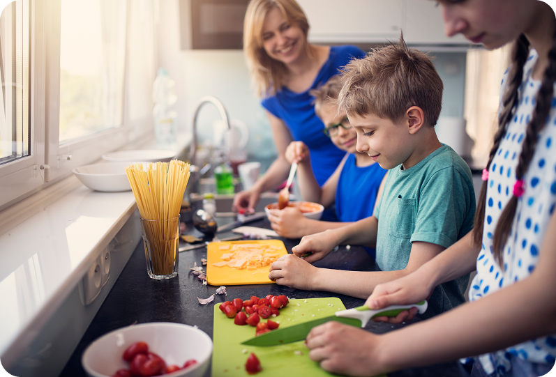 Children and adult preparing meals together in a kitchen, engaging in cooking activities, fostering skill mastery and independence, aligned with Ability to Achieve's focus on personal care and community access.