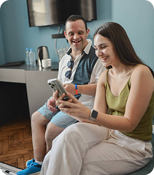 Smiling young man and woman engaging with a smartphone in a bright, comfortable setting, representing inclusive disability support and community connection in Parramatta.