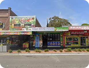 Colorful storefronts of Tolo Kebab House and nearby market, showcasing fresh produce and grocery items, reflecting the diverse community in Western Sydney.