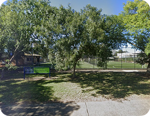 Community park setting with a large tree, grassy area, and sports field in the background, representing areas serviced by Ability to Achieve for disability support in Sydney.