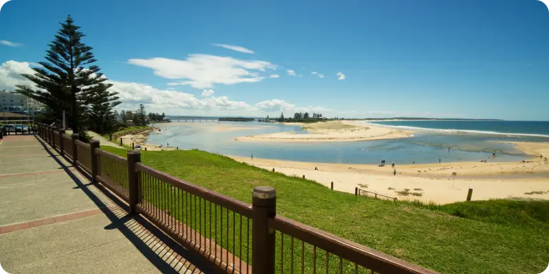 Scenic view of The Entrance, Central Coast, featuring a sandy beach, calm waters, and a promenade with greenery, illustrating the local coastal lifestyle and community connection.