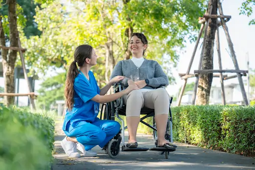 Support worker assisting a woman in a wheelchair outdoors, emphasizing person-centered care in disability support services.