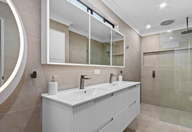 Modern bathroom design featuring dual sinks, large mirrors, and a glass shower enclosure, emphasizing a clean and spacious aesthetic suitable for supported accommodation services.