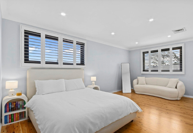 Modern bedroom with a plush bed, natural light from large windows, minimalist decor, and a cozy seating area, reflecting a comfortable living space for supported accommodation.