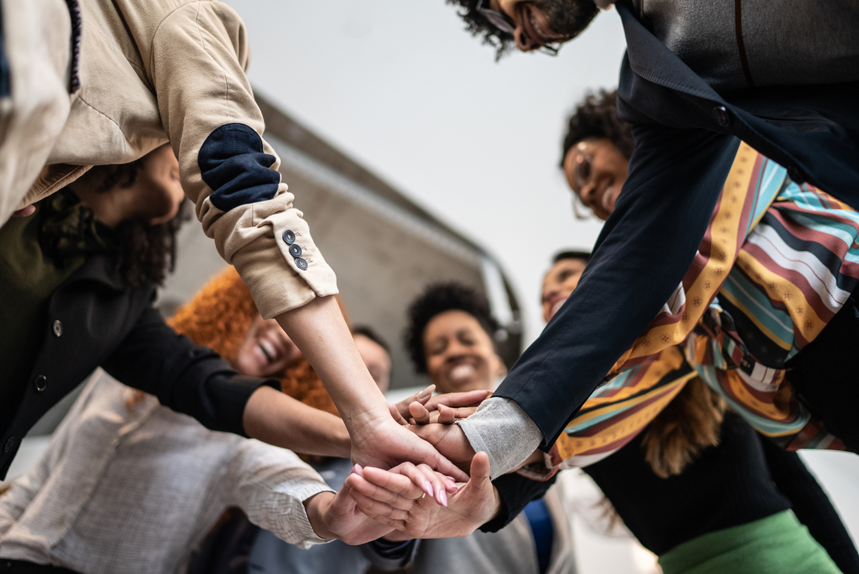 Group of diverse individuals joining hands in a supportive gesture, symbolizing community involvement and teamwork in supported independent living.