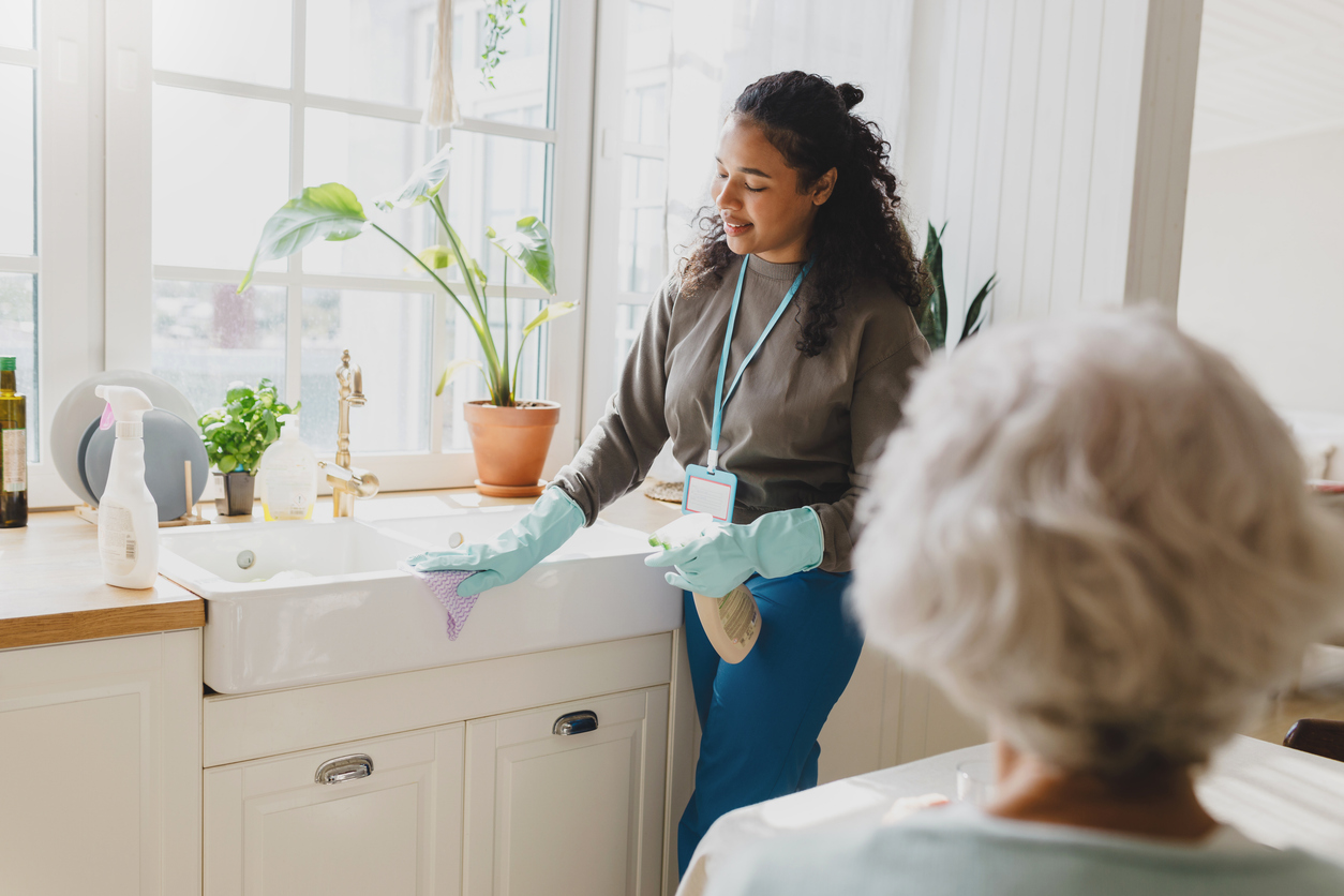 Support worker assisting with household cleaning tasks in a bright kitchen, promoting independence and personal care for individuals in supported living environments.