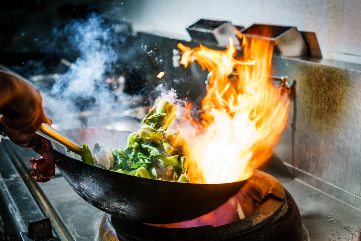 Wok cooking with vibrant flames and vegetables, illustrating skill development in cooking for supported independent living.