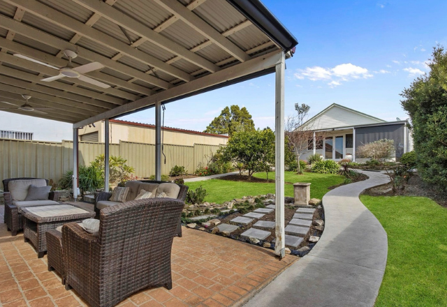 Outdoor space featuring a covered patio with wicker seating, landscaped garden, and pathway leading to a residence, reflecting a welcoming environment for supported accommodation services.