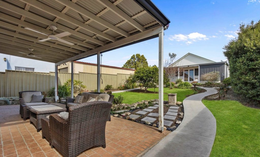 Outdoor seating area under a covered patio, featuring wicker furniture, surrounded by a landscaped garden with pathways, enhancing the supportive independent living environment at Ability to Achieve.