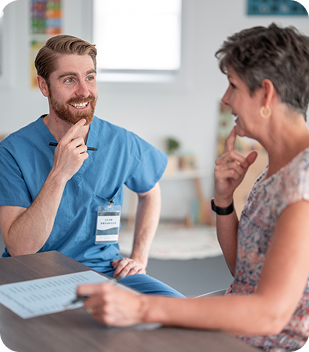 Healthcare professional in scrubs engaging in conversation with a client, discussing speech therapy services in a supportive environment.