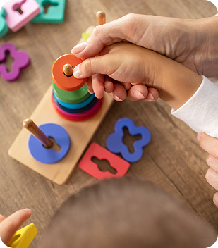 Child and adult hands engaging with colourful stacking toy, promoting developmental skills and independence, relevant to Ability to Achieve's focus on empowering individuals in Canberra.