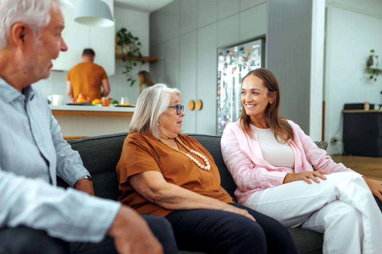 Group of three adults engaged in conversation on a sofa, discussing NDIS services, with a kitchen setting in the background.