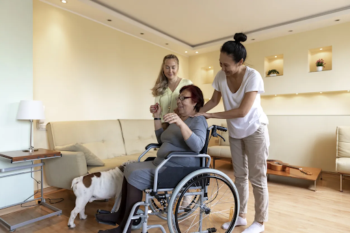 Woman in wheelchair receiving assistance from two caregivers in a bright, accessible living space, highlighting support for independent living under NDIS housing solutions.