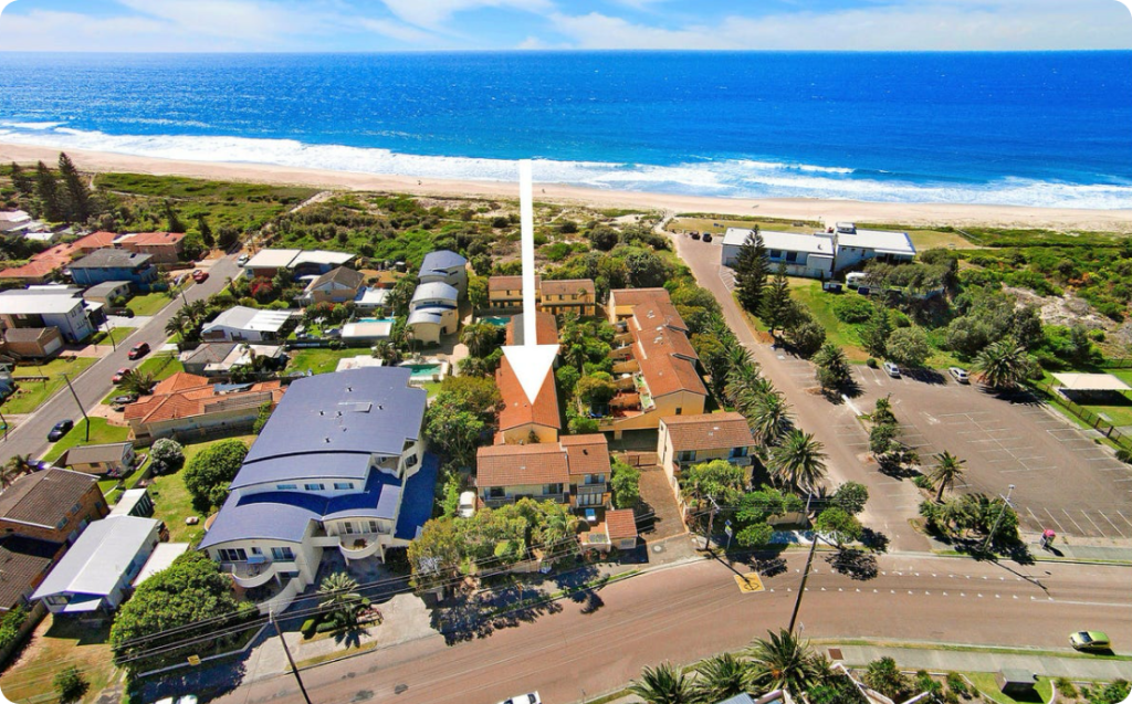 Aerial view of supported accommodation properties near Central Coast, NSW, showcasing residential buildings, palm trees, and proximity to the beach and community amenities.